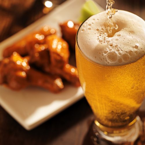 Pouring,Beer,With,Chicken,Wings,In,Background.